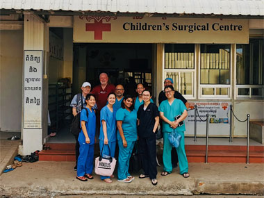 A group of doctors and nurses taking a photo in front of a Children's Surgical Centre.