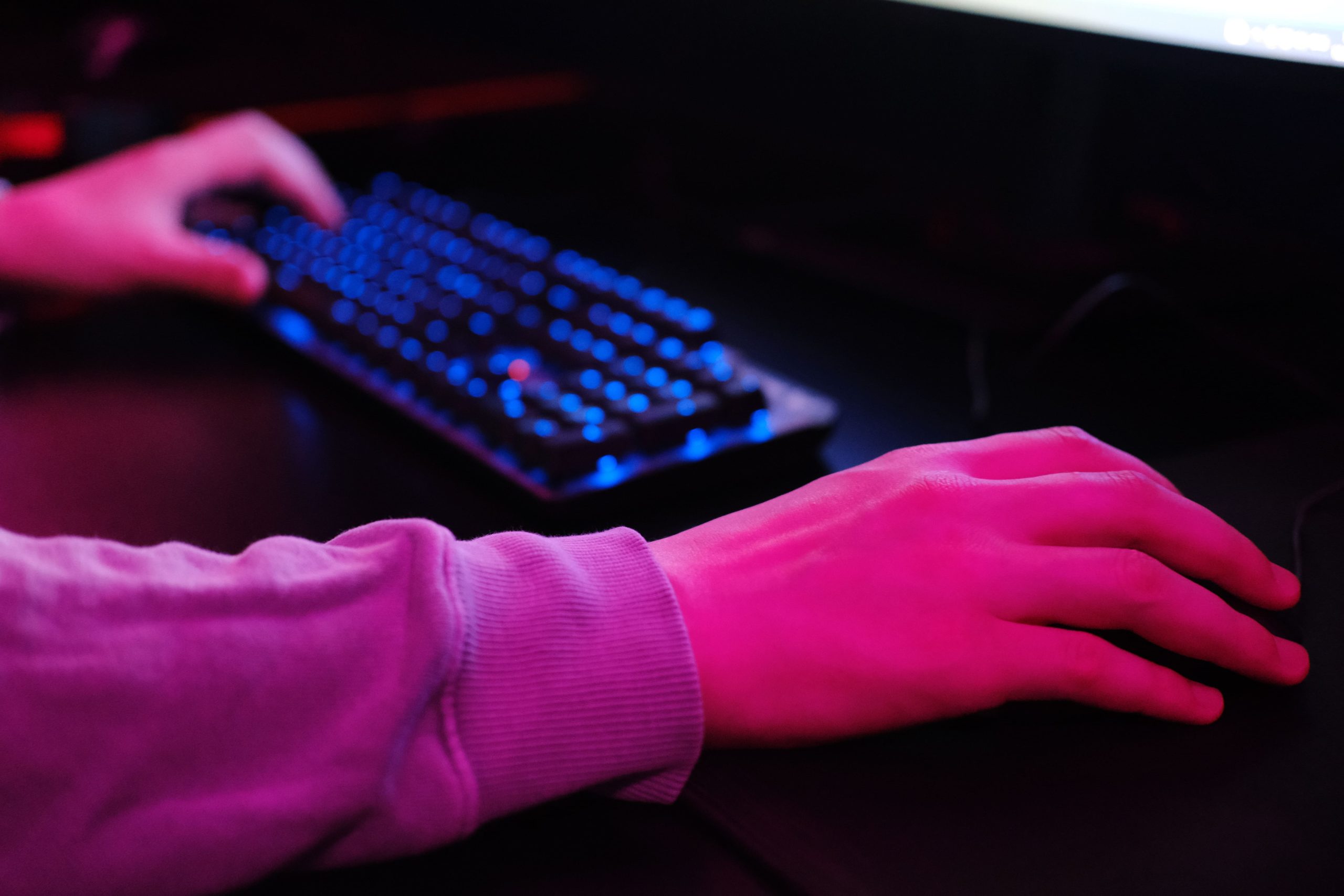 A close-up view of a hand reaching for a computer mouse with a colorful illuminated keyboard in the background.