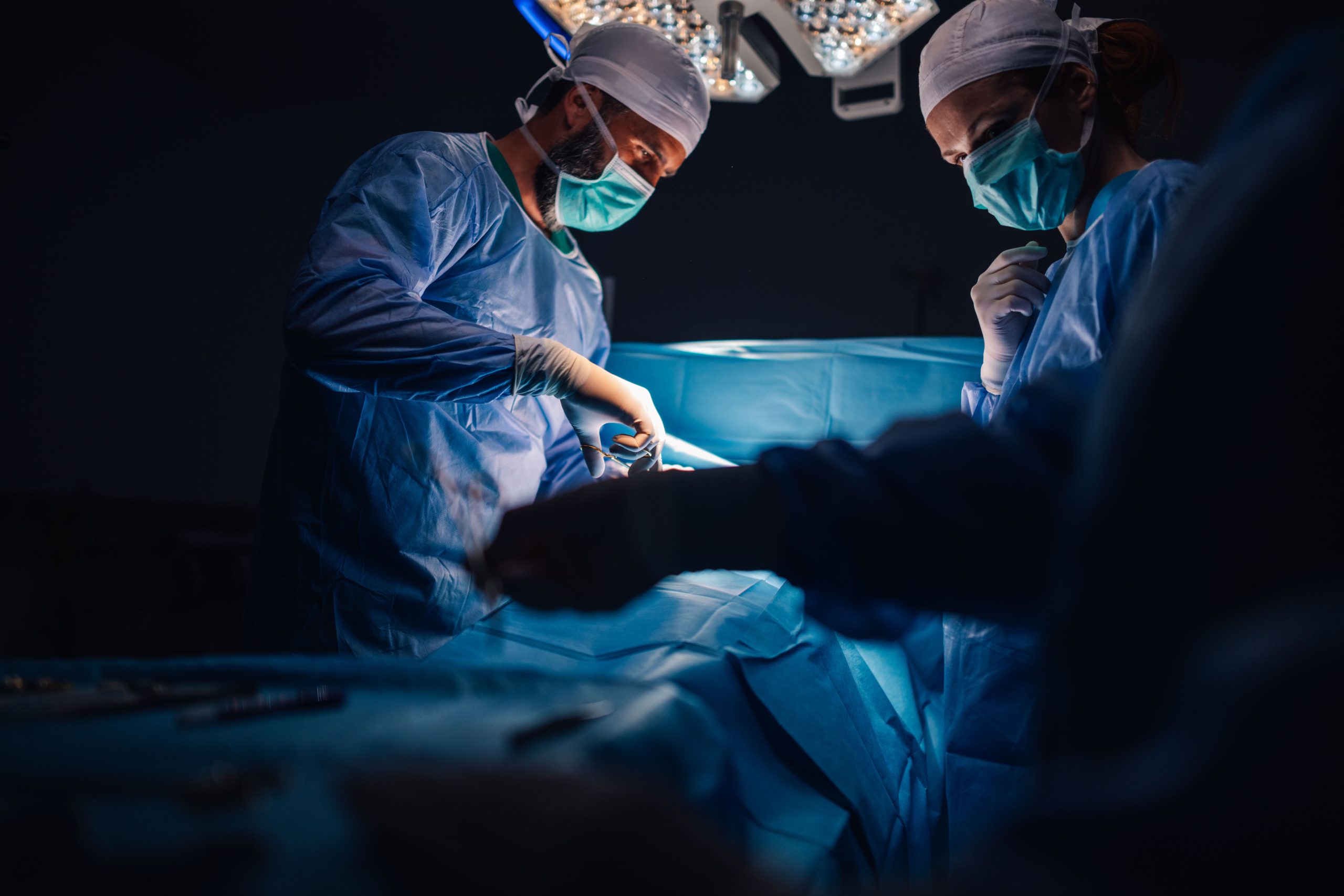 A medical team performing surgery in an operating room, wearing surgical attire and focused on the procedure.