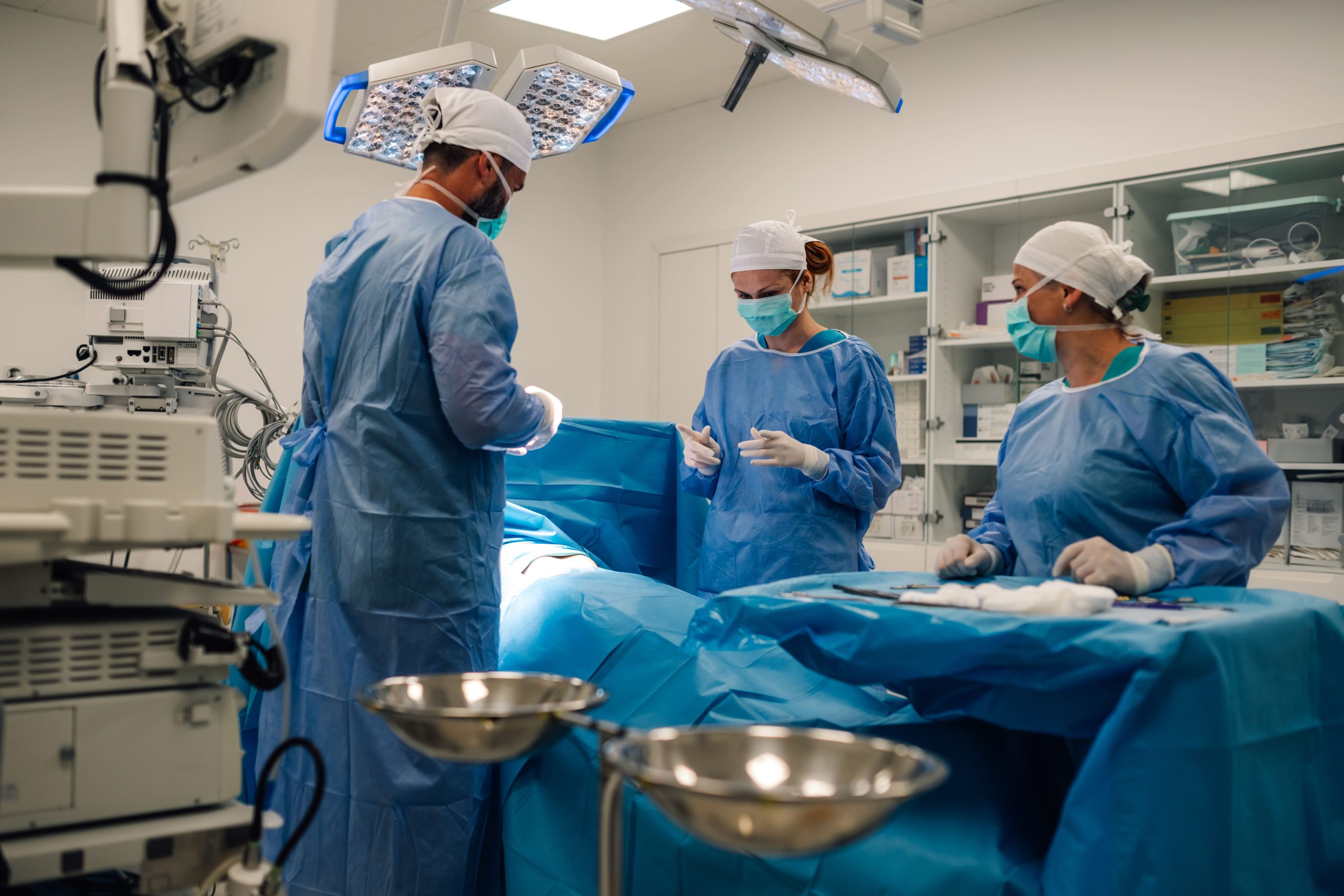 Medical professionals in blue surgical gowns preparing for a hand surgery in an operating room.